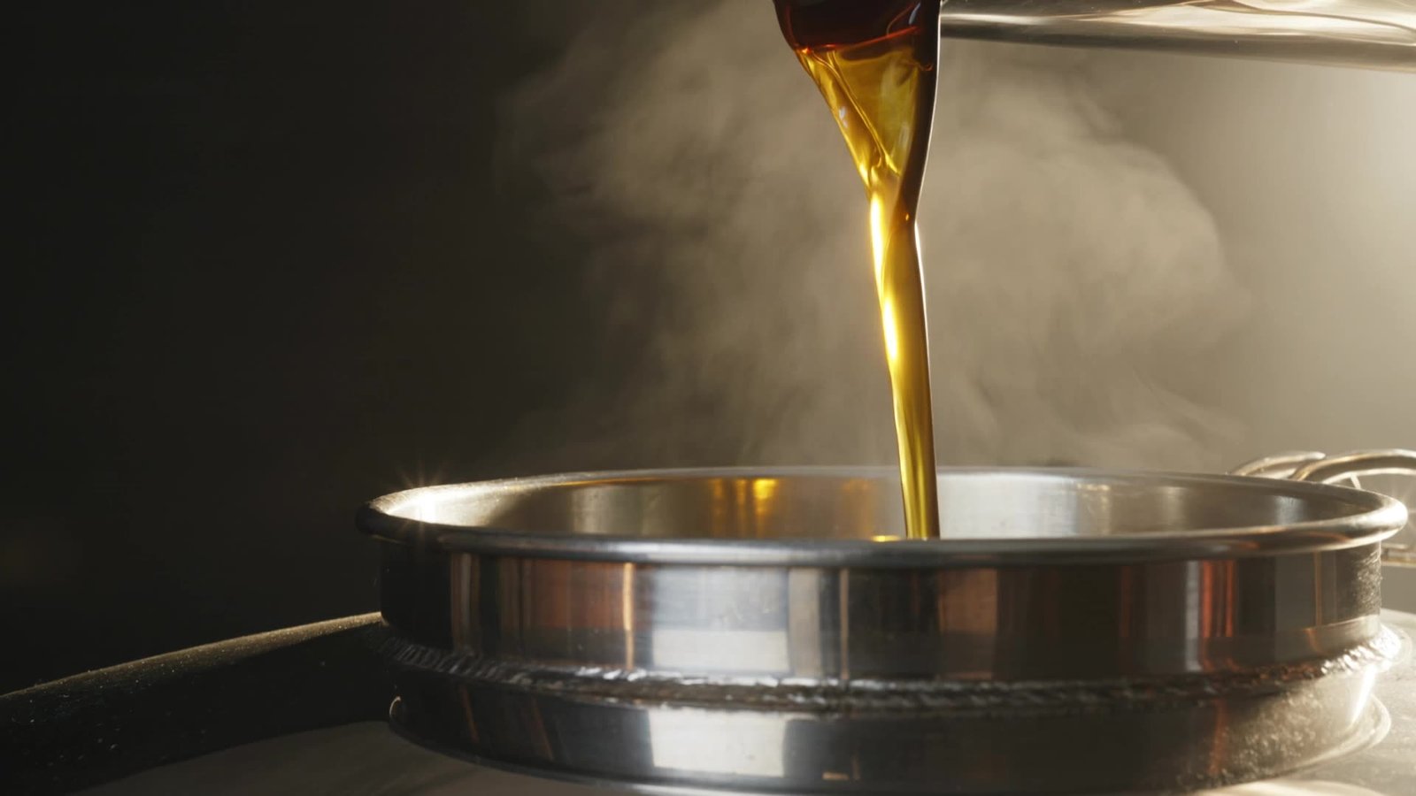 Golden palm oil pouring into a steel processing vessel