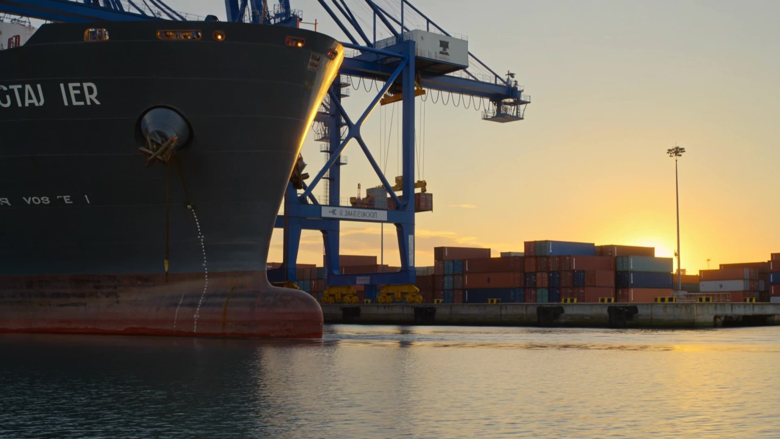 Container ship docked beneath gantry cranes at sunset